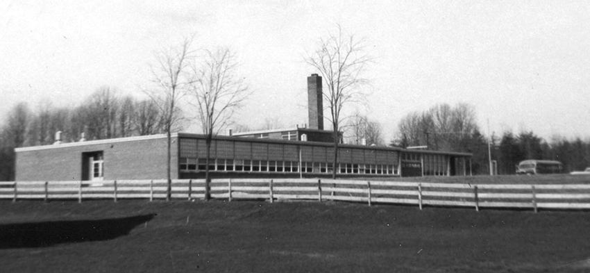 Black and white photograph of Lemon Road Elementary School taken in 1958. Idylwood Road is much narrower than in the present day and there are less trees. A white fence separates the school property from neighboring homes.